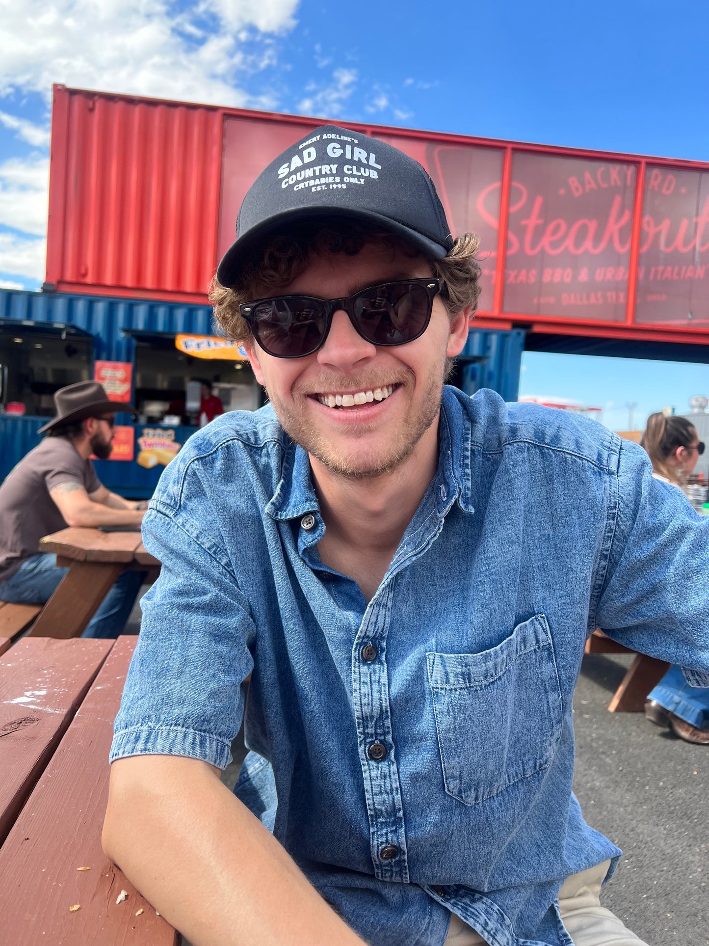 Handsome man wears black trucker hat with text "Emery Adeline's Sad Girl Country Club Crybabies Only Est. 1995"